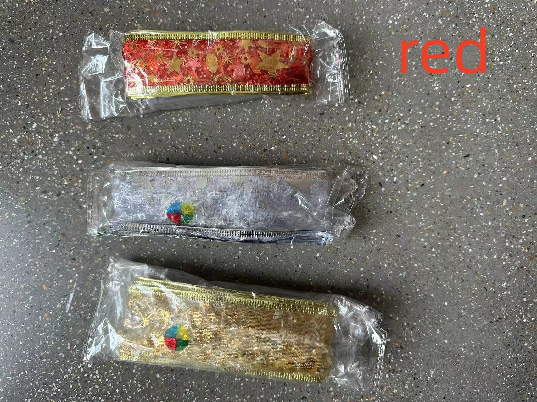Three decorative metallic ribbon rolls in red, silver, and gold packaging on a speckled surface with red text 'red'