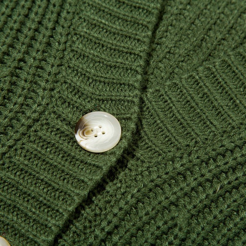 Close-up of green knitted sweater with textured ribbed pattern and round beige button