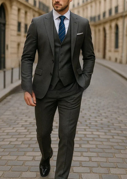 Man wearing a tailored dark gray three-piece suit with a blue striped tie walking on a cobblestone street