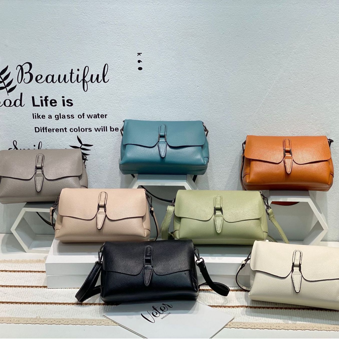 Seven colorful leather crossbody bags displayed on white hexagonal shelves with decorative wall text
