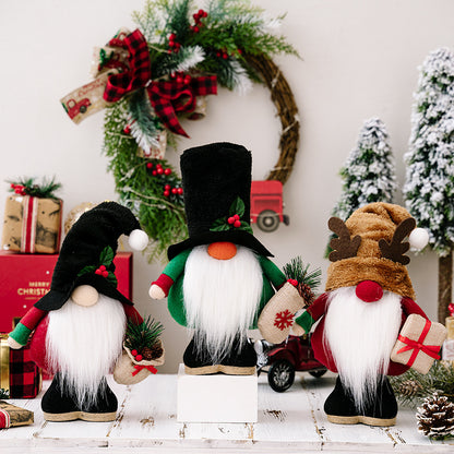 Three Christmas gnome decorations with long white beards and festive hats on wooden surface, pine wreath and snowy trees background