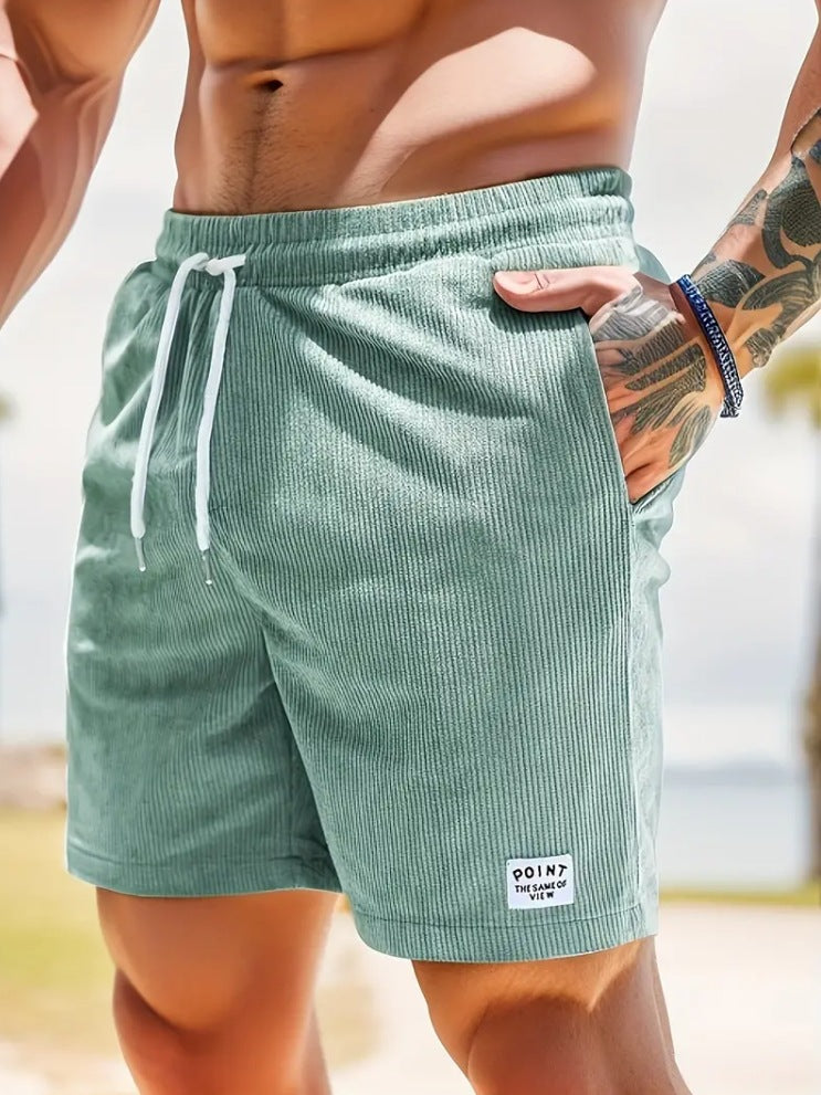 Man wearing light green ribbed shorts with white drawstring and tattooed arm outdoors