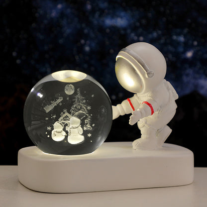 White astronaut figurine with lighted snow globe depicting snowmen and Christmas tree on white base