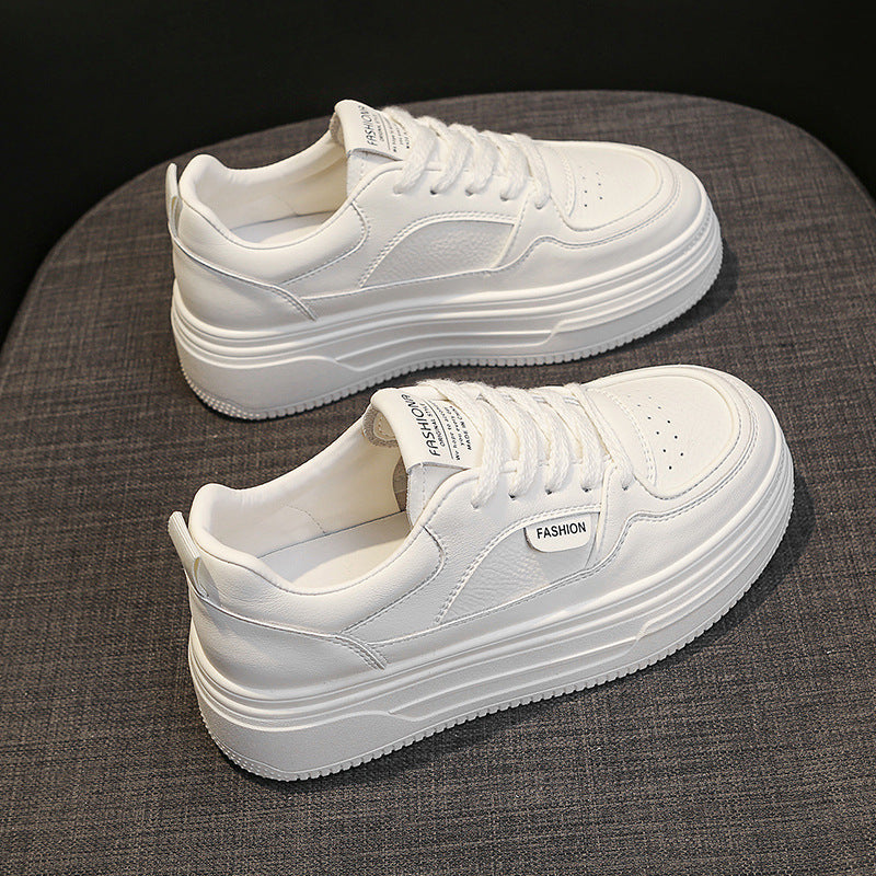Pair of white platform sneakers with laces and fashion label on gray fabric surface