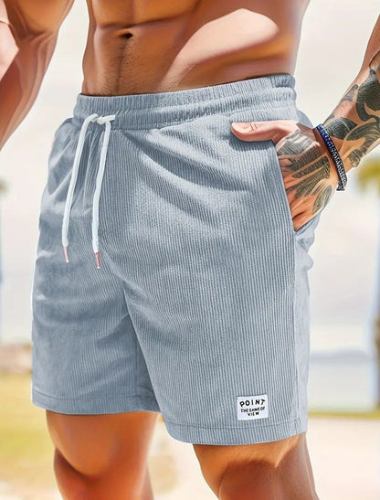 Close-up of muscular man wearing light gray ribbed drawstring shorts with side pocket and tattooed arm