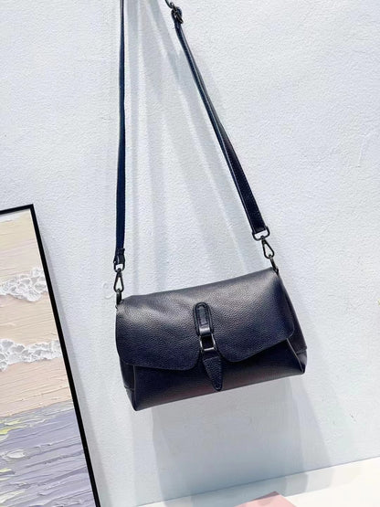 Black leather crossbody bag with buckle detail hanging on white wall