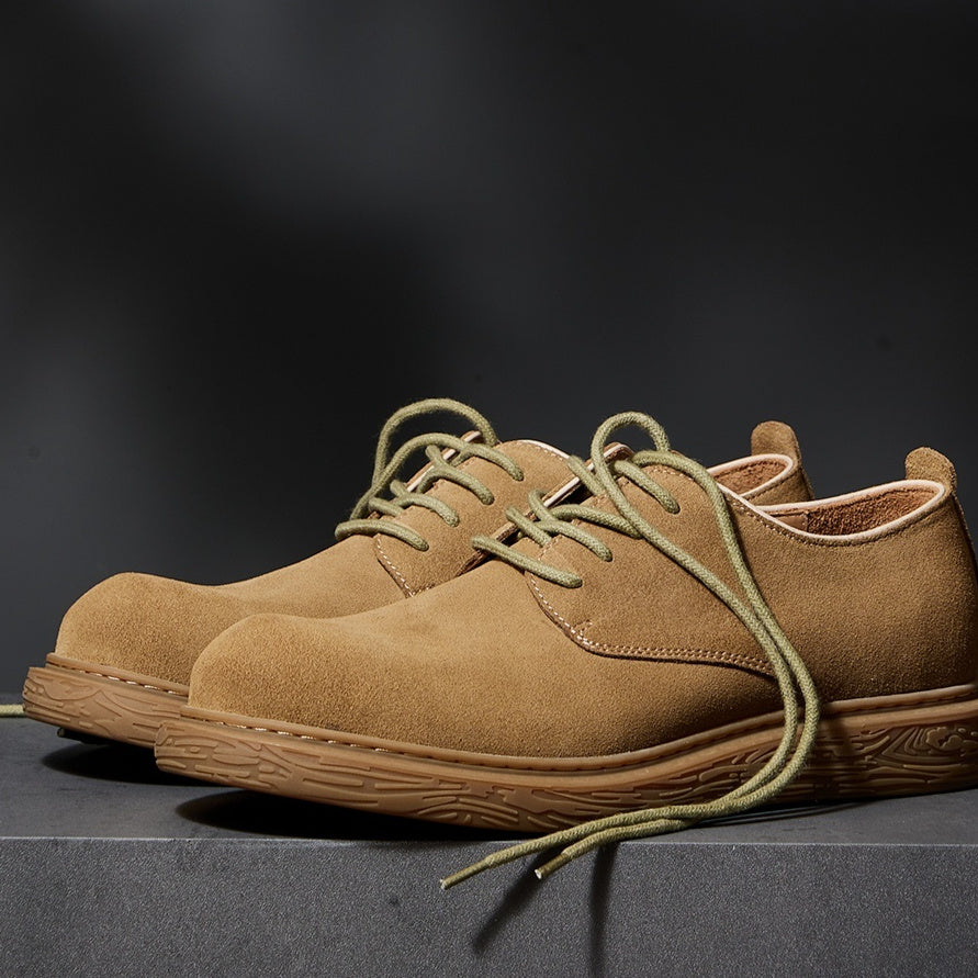 Pair of tan suede casual shoes with green laces on a grey surface and dark background