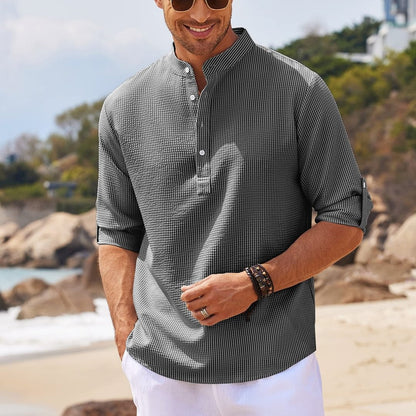 Man wearing striped mandarin collar shirt with rolled sleeves and white shorts on beach
