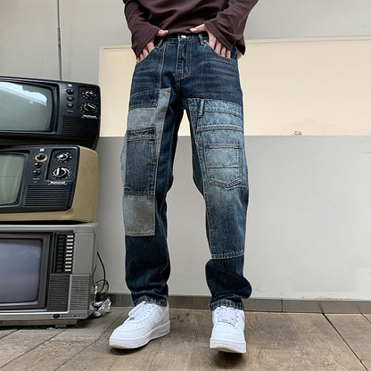 Man wearing dark patchwork jeans and white sneakers standing on wooden floor near stacked vintage TVs