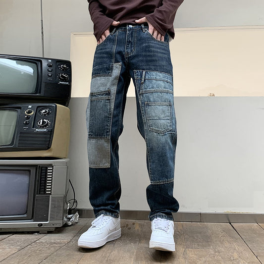 Man wearing dark patchwork jeans and white sneakers standing on wooden floor near stacked vintage TVs