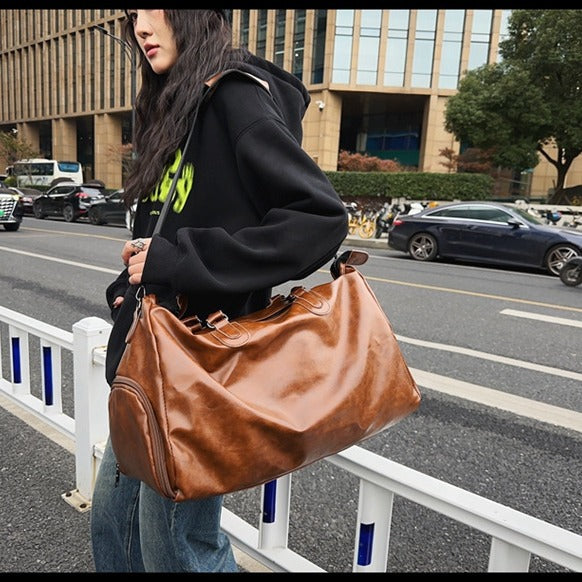 Woman wearing black hoodie and jeans carrying a large brown leather duffle bag on city street