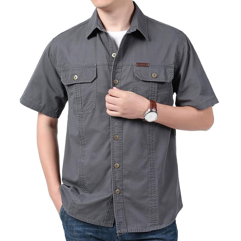 Man wearing gray short-sleeve button-up shirt with flap pockets and blue jeans on white background