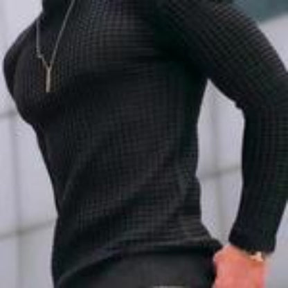 Person wearing a fitted black ribbed sweater and a silver pendant necklace against a blurred background