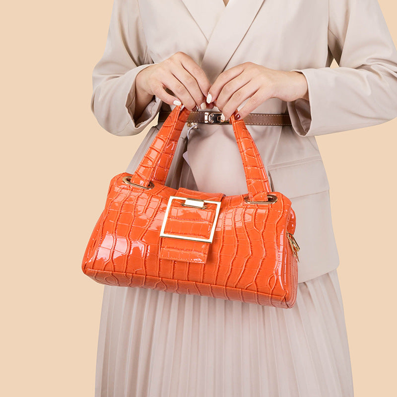 Woman wearing beige suit holding orange crocodile pattern handbag with gold buckle
