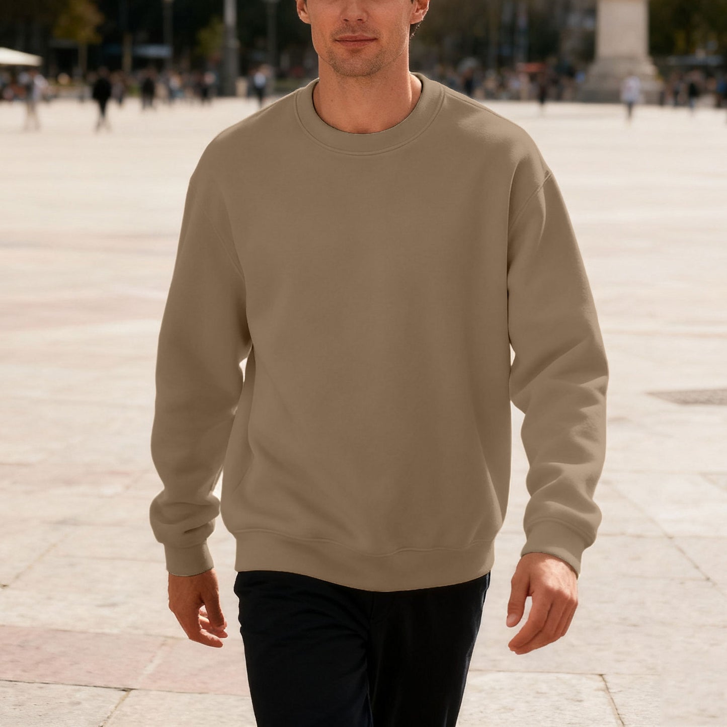 Man wearing beige crewneck sweatshirt walking outdoors in urban plaza with people in background