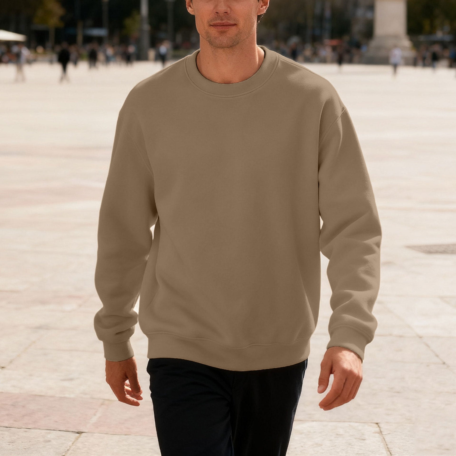 Man wearing beige crewneck sweatshirt walking outdoors in urban plaza with people in background