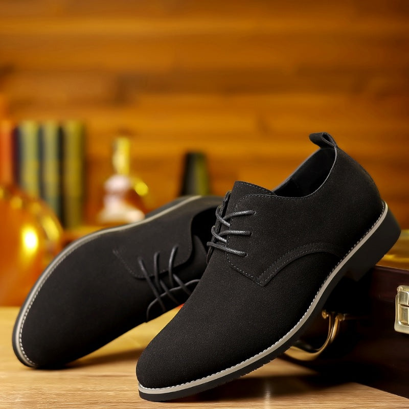 Black suede men's dress shoes with laces on wooden surface and blurred wooden background