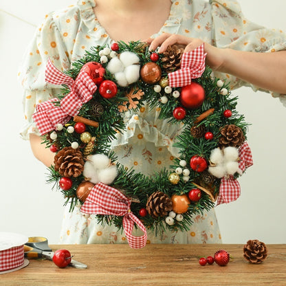 Woman holding handmade Christmas wreath decorated with pinecones, red berries, cotton, and checkered red bows