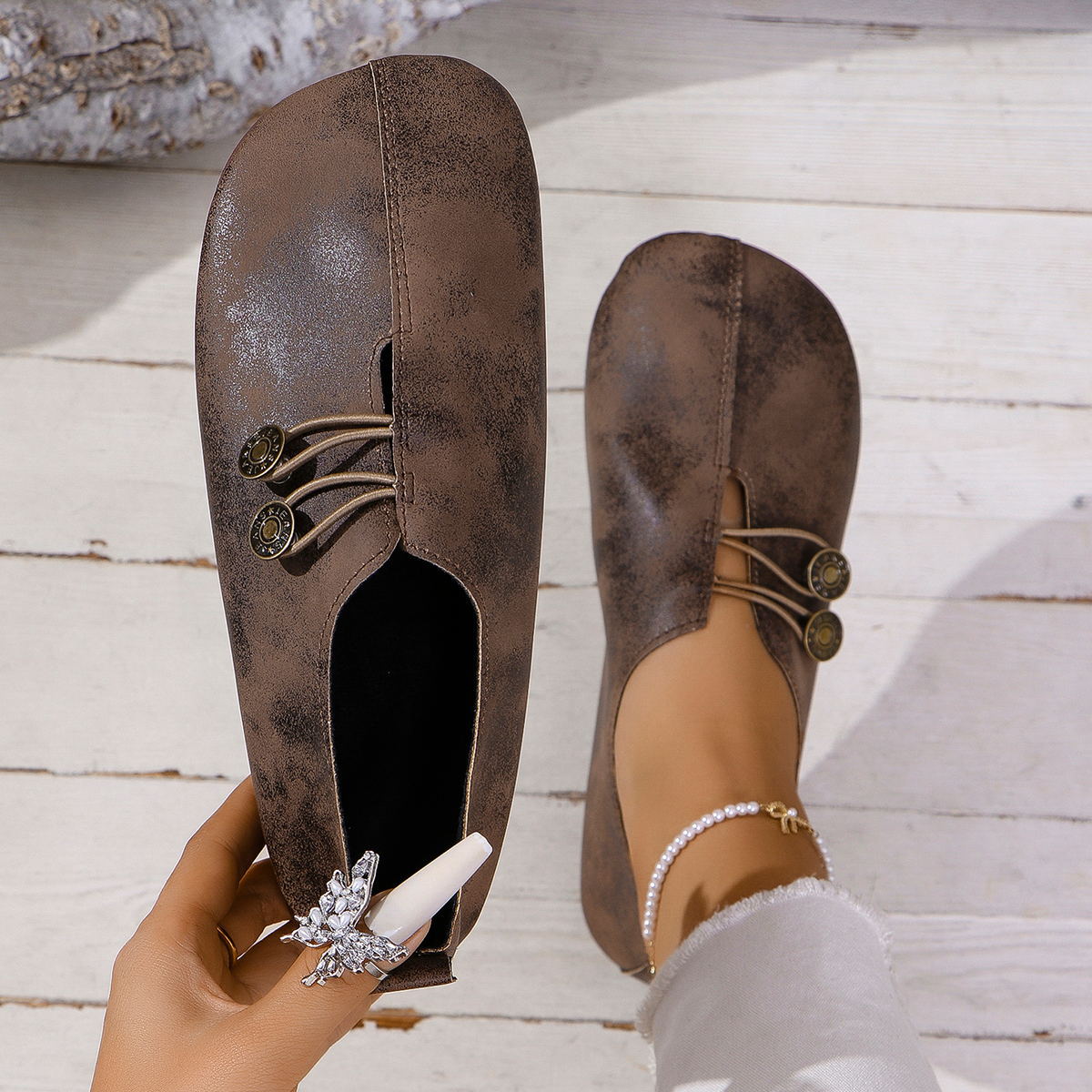 Brown distressed vintage-style slip-on shoes with button accents on wooden floor