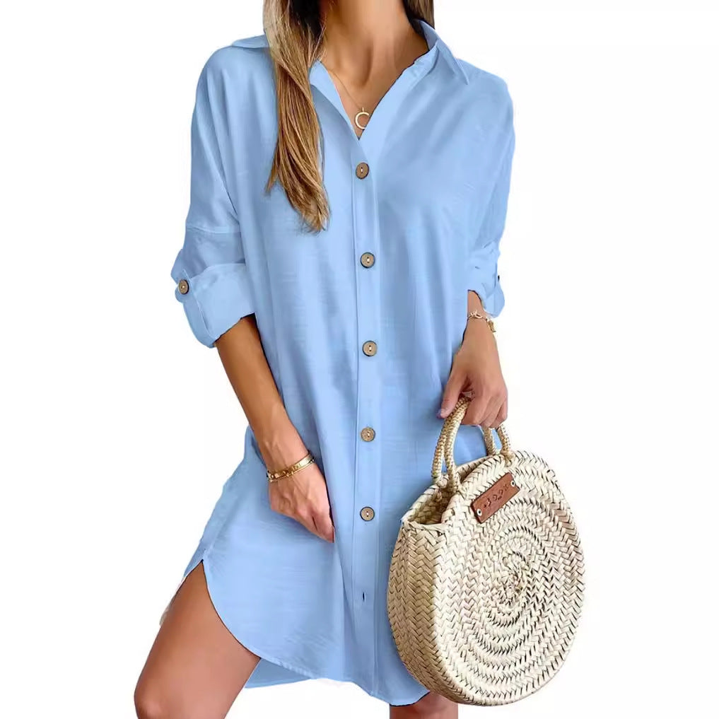 Woman wearing light blue button-up shirt dress with rolled sleeves, holding round woven straw handbag