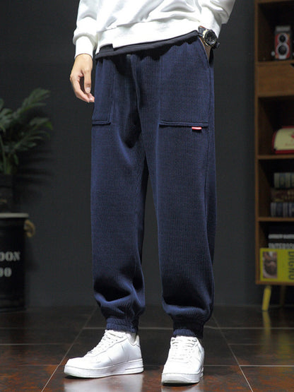 Men's navy blue corduroy jogger pants with pockets paired with white sneakers and a white sweatshirt