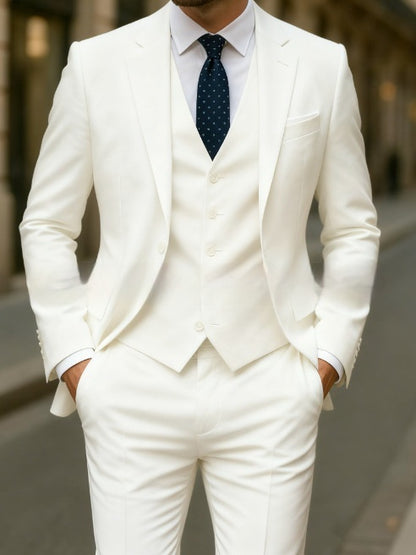 Man wearing a tailored white three-piece suit with a navy blue polka dot tie, hands in pockets