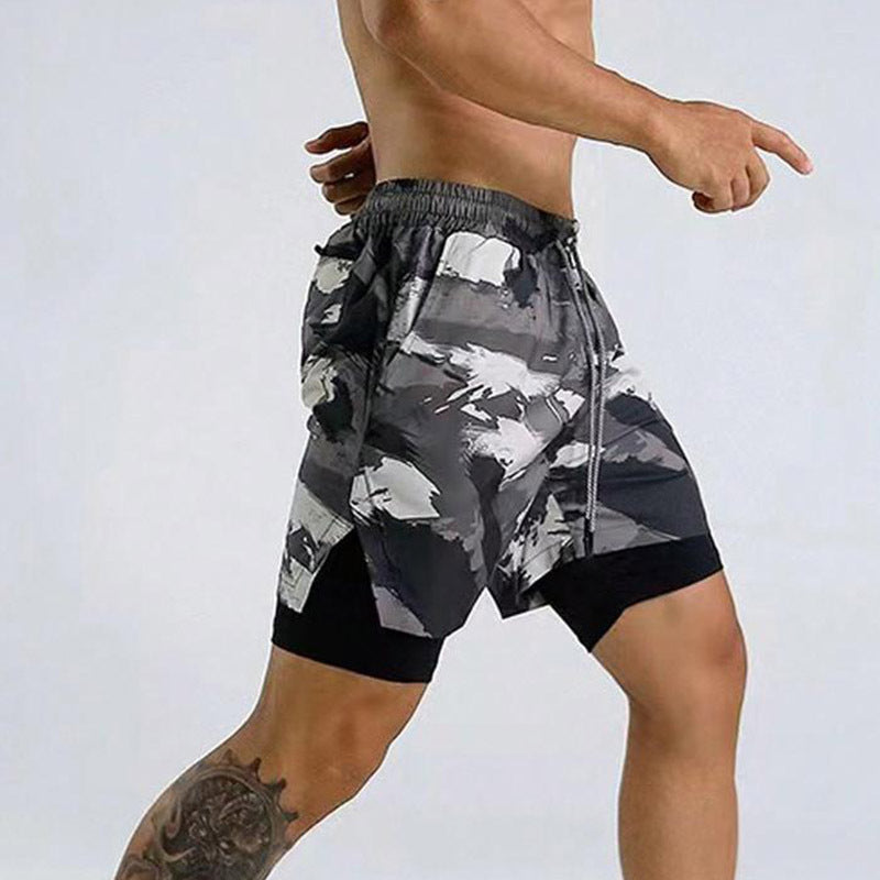 Male model wearing black and gray camo print athletic shorts with inner compression layer and drawstring waistband