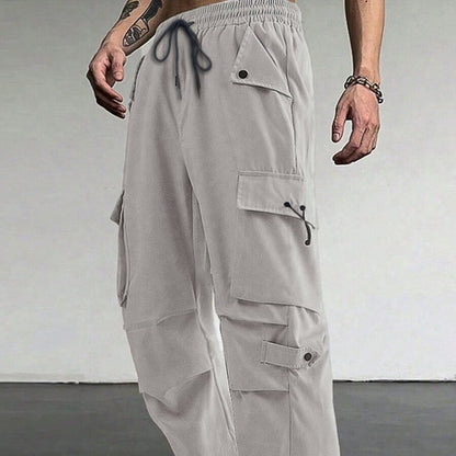 Man wearing light gray cargo pants with multiple pockets and black drawstring in minimalist setting