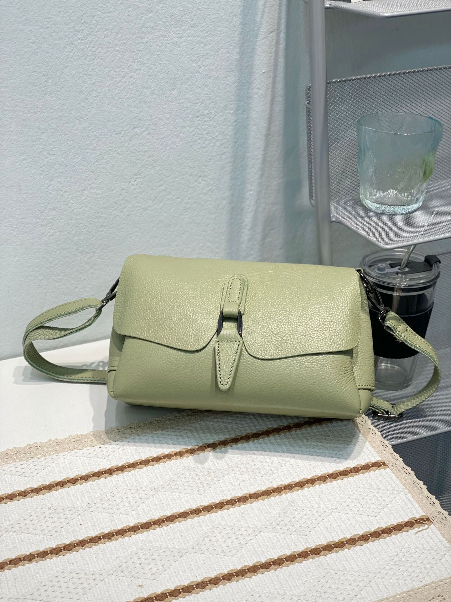 Light green pebble leather crossbody bag on a white textured fabric with brown stripes