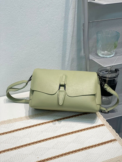 Light green pebble leather crossbody bag on a white textured fabric with brown stripes