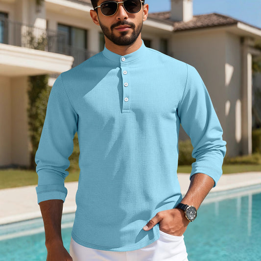 Man wearing light blue textured henley shirt and sunglasses by a pool with house background