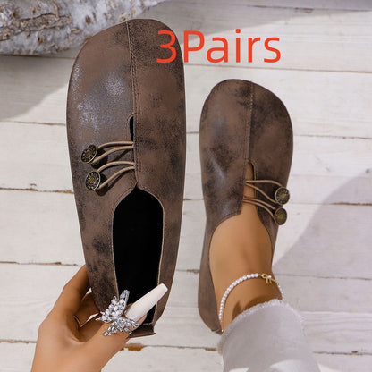 Pair of brown vintage-style flat shoes with decorative metal buttons on wooden floor