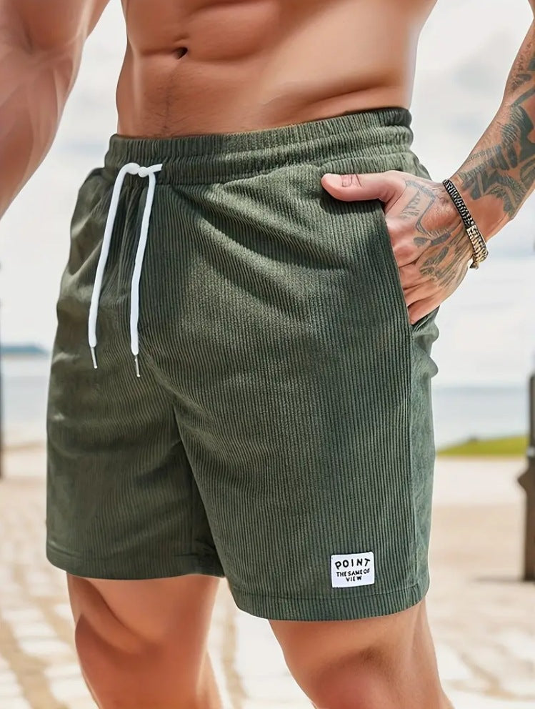 Close-up of muscular man wearing olive green drawstring shorts with ribbed texture and tattooed arm by waterfront