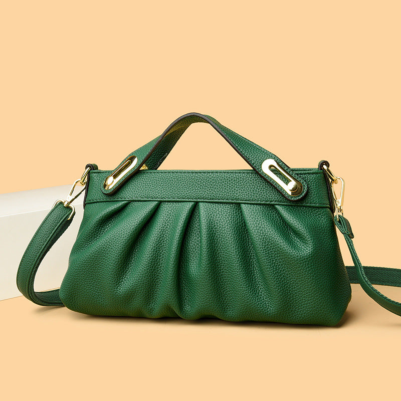 Green leather handbag with gold hardware and detachable shoulder strap on beige background