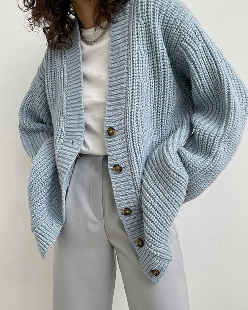Woman wearing light blue chunky knit cardigan with brown buttons over white top and beige pants