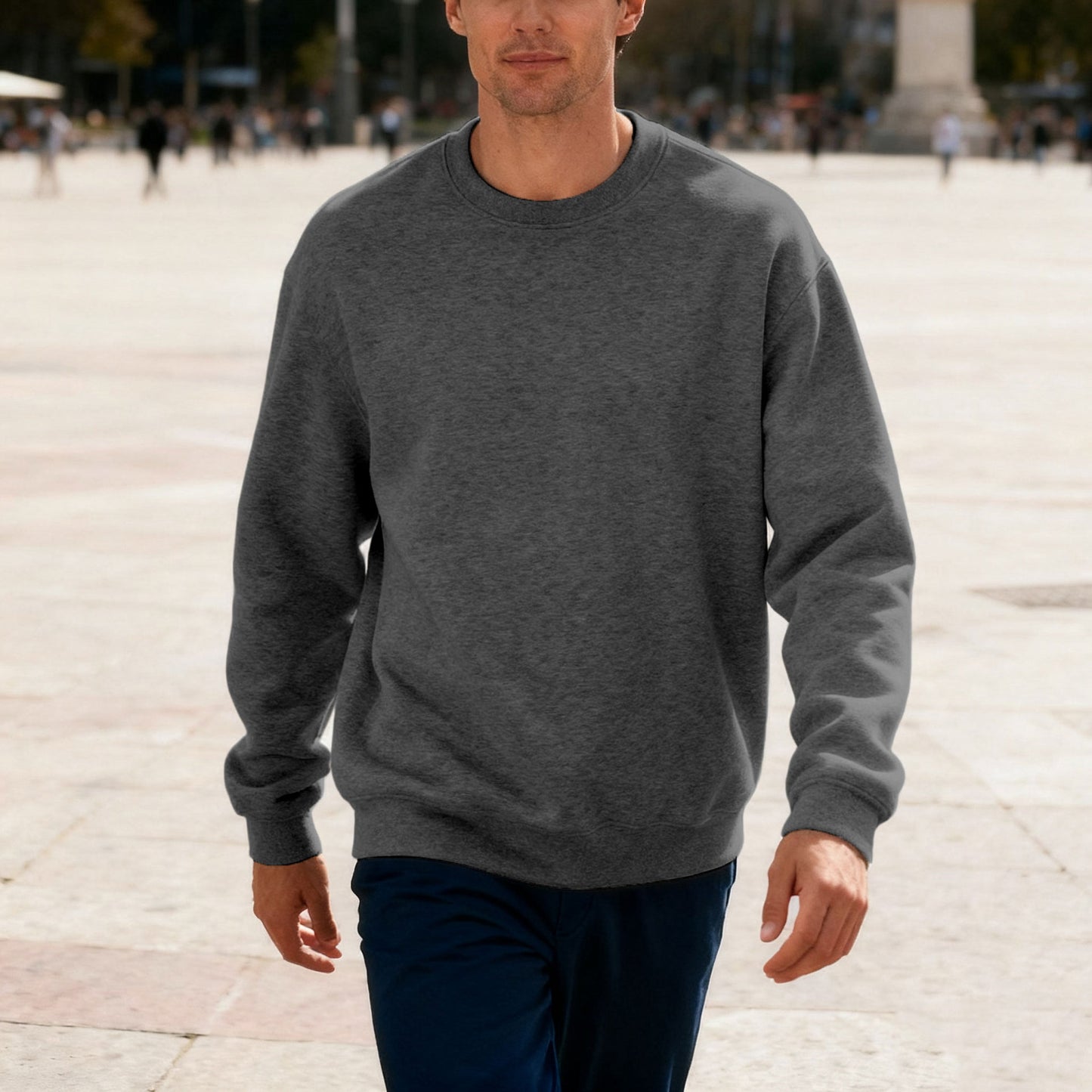 Man wearing dark gray crewneck sweatshirt and navy pants walking outdoors on sunny day