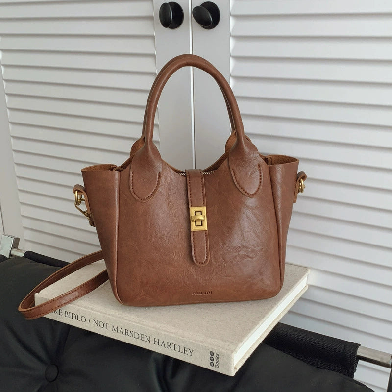 Brown leather handbag with gold clasp on a book against white louvered closet doors