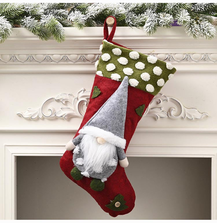 Red Christmas stocking with white and green polka dot cuff, hanging on mantel with snow-dusted pine garland, featuring a gray gnome with a white beard