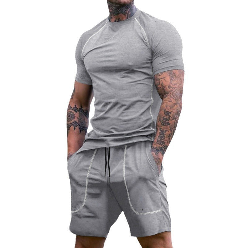 Muscular man with tattoos wearing fitted light gray short-sleeve athletic t-shirt and matching shorts with pockets