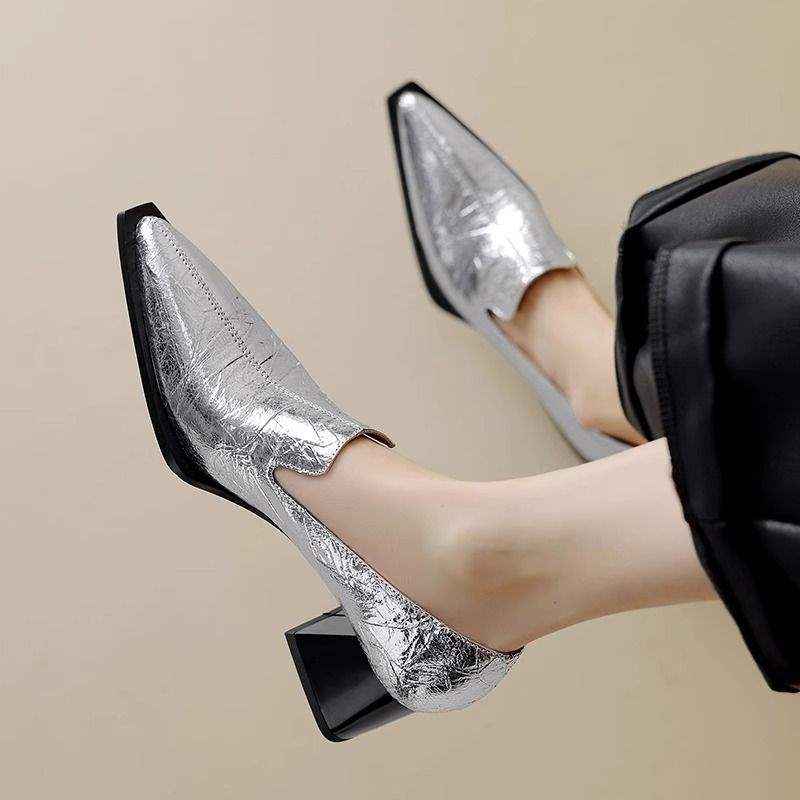 Stylish women's silver metallic pointed toe block heel shoes worn with black pants on beige background