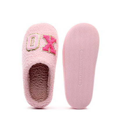 Soft pink fuzzy slippers with 'OX' embellishment and textured non-slip sole on white background