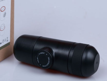 Black portable coffee grinder with adjustable dial on white surface next to cardboard packaging