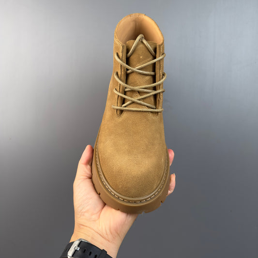 Hand holding a tan suede leather boot with beige laces and a brown rubber sole against gray background