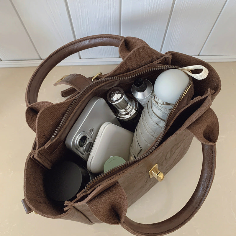 Overhead view of a brown leather handbag containing a smartphone, compact mirror, lipstick, umbrella, and cosmetic jar