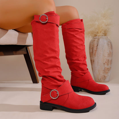 Red knee-high suede boots with silver buckle straps worn by seated model next to decorative vase
