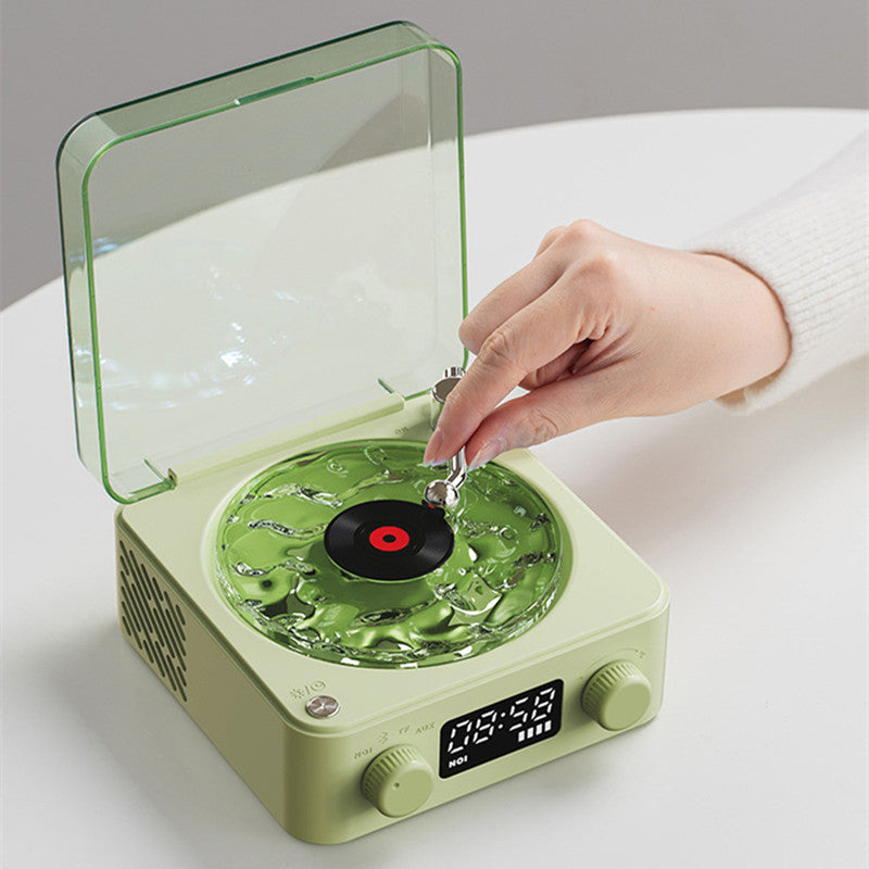 Hand operating small green retro-style record player with clear cover and digital display on white table
