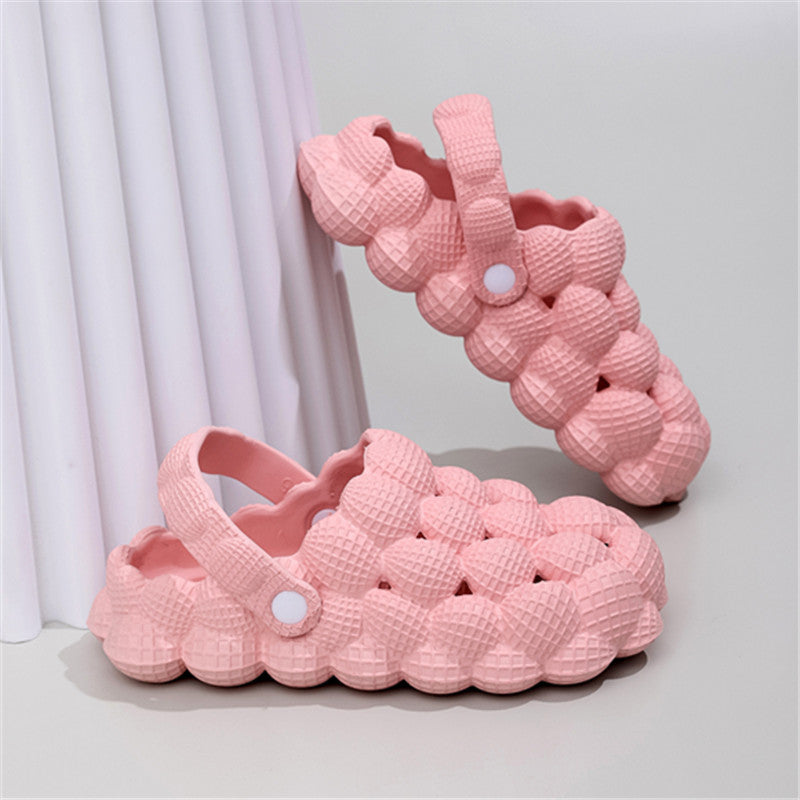 Pink bubble-textured foam clogs with adjustable strap on neutral background