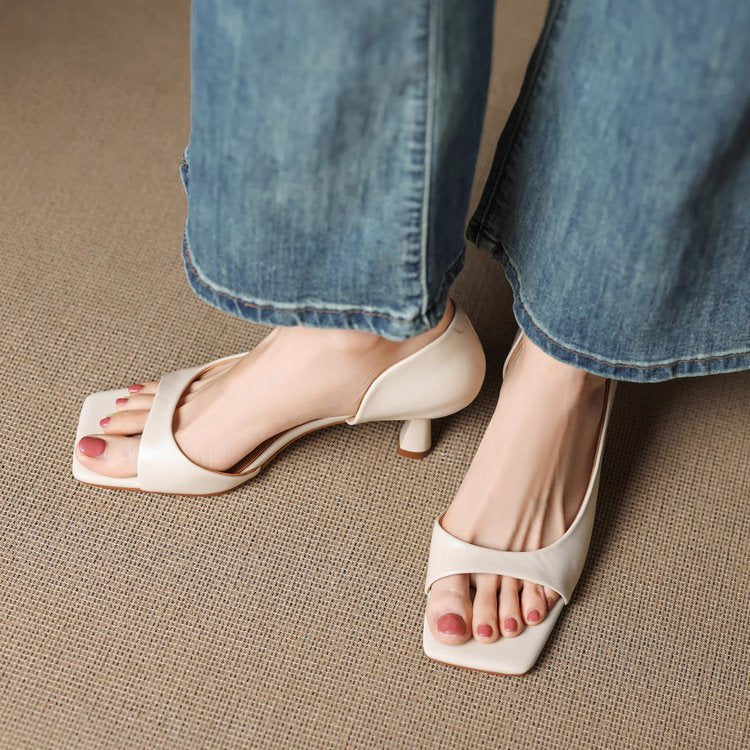 Pair of stylish beige open-toe block heel sandals worn with cropped blue jeans on textured surface