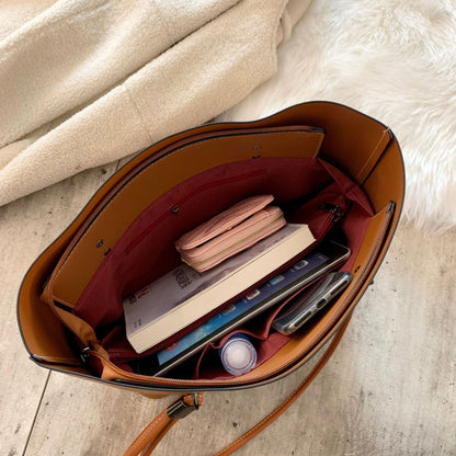 Open brown leather handbag showing organized interior with wallet, book, tablet, phone, and water bottle