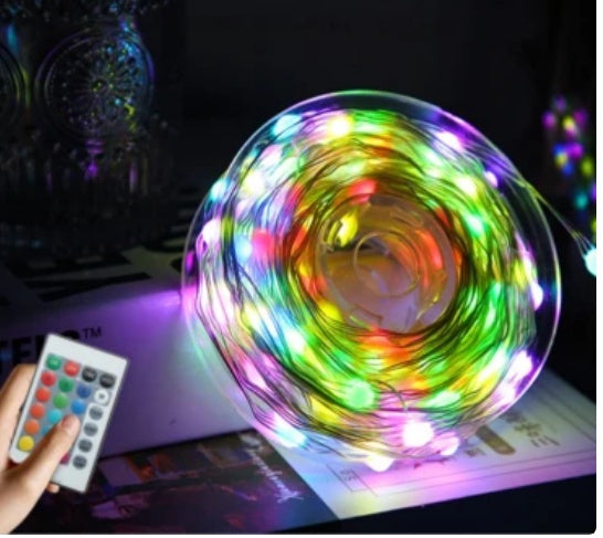 Multicolor LED Christmas tree string lights coiled on a surface with a hand holding a remote control